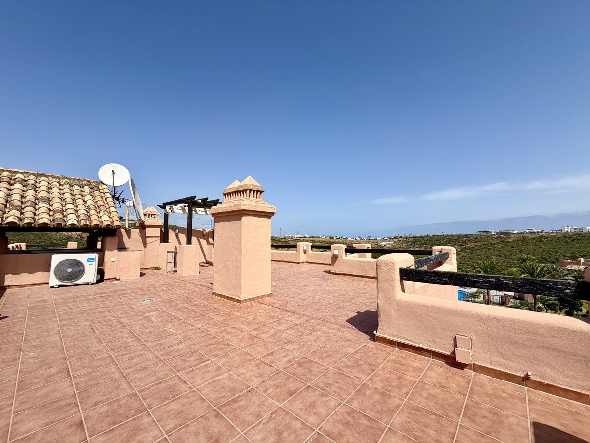 Terrace with air conditioning unit, chimney, and distant sea view under a clear blue sky.