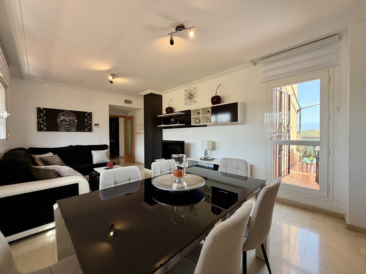 Modern living and dining area with a large sofa, dining table, and a balcony with a sea view.
