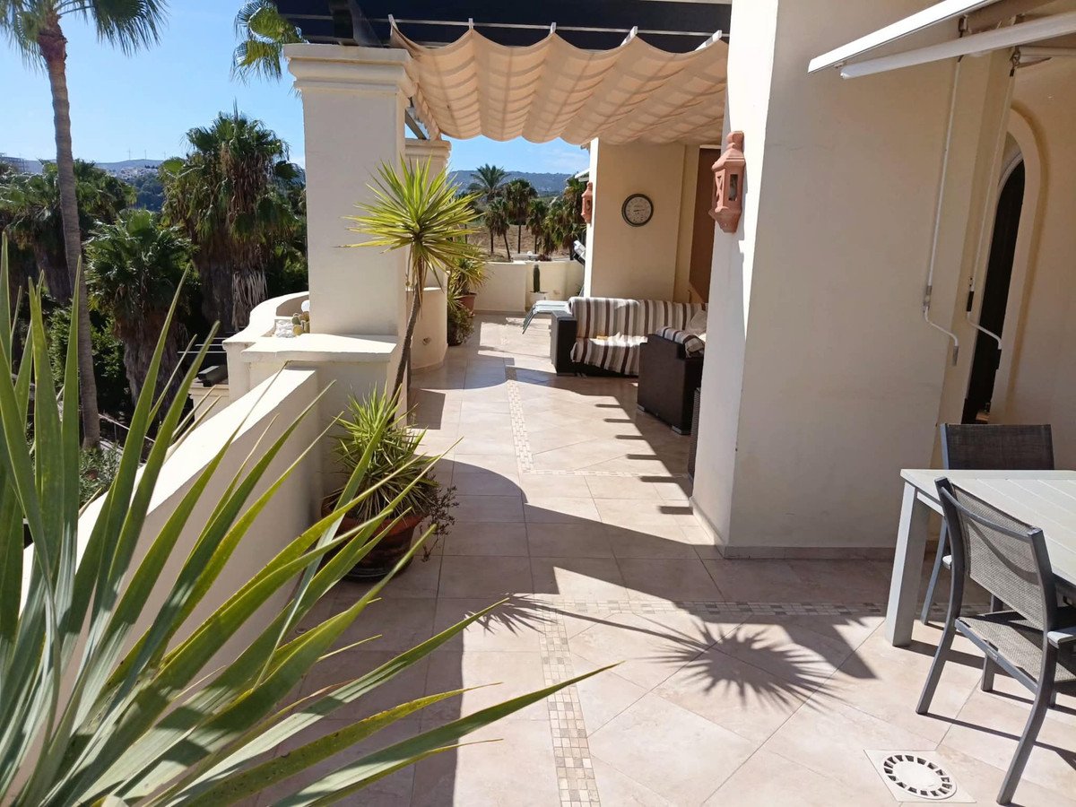 A spacious tiled terrace with seating areas, outdoor dining, and lush greenery, offering scenic views under a retractable awning.