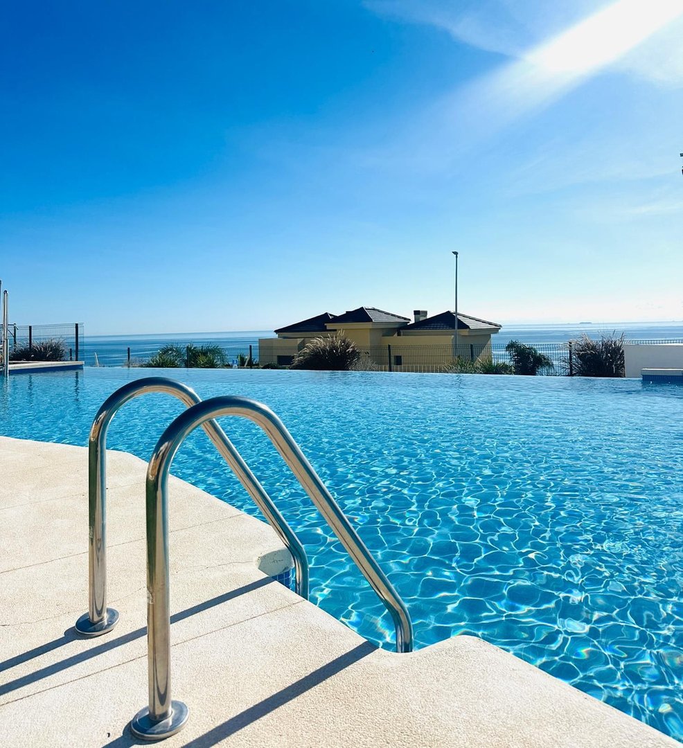 Infinity swimming pool with chrome ladder and a stunning view of the ocean and houses.