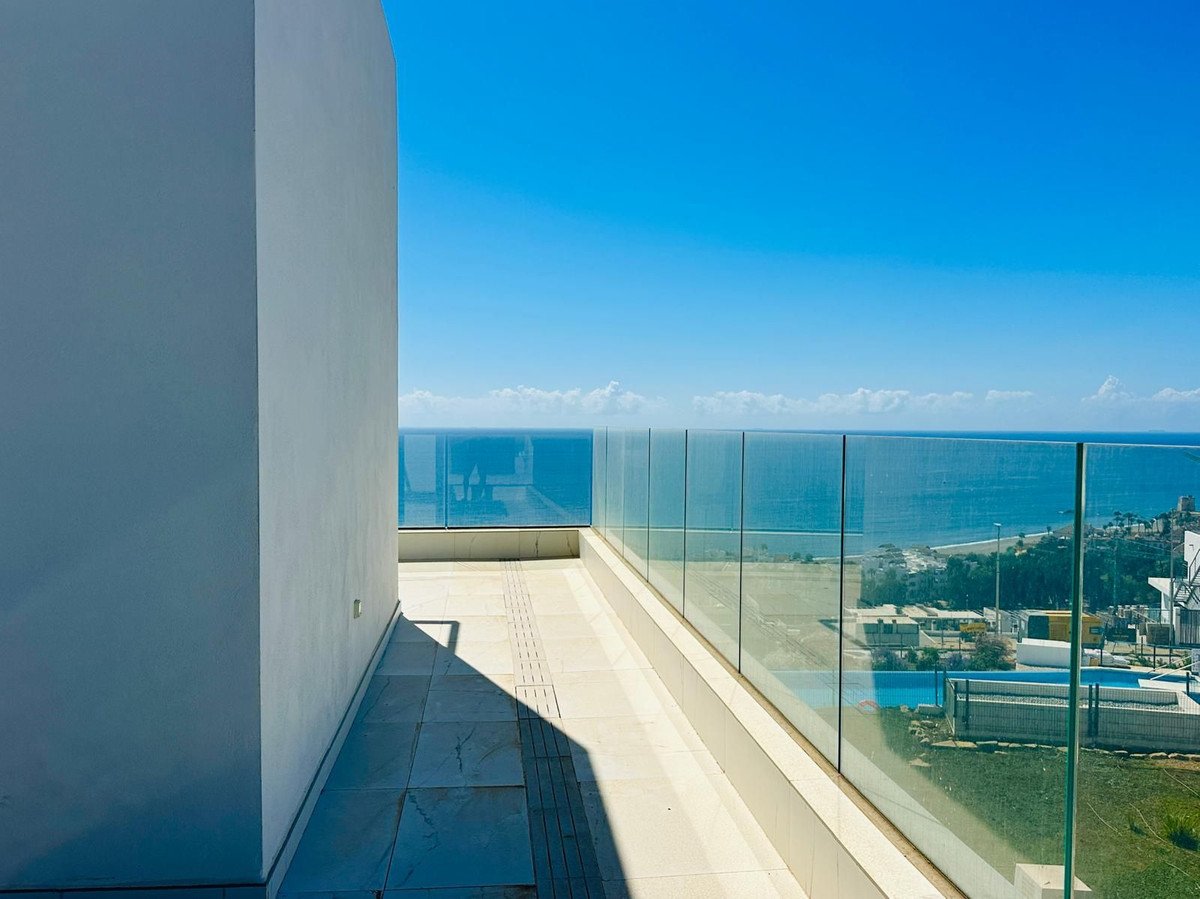 Modern balcony with glass railings offering panoramic views of the sea and coastline on a clear sunny day.