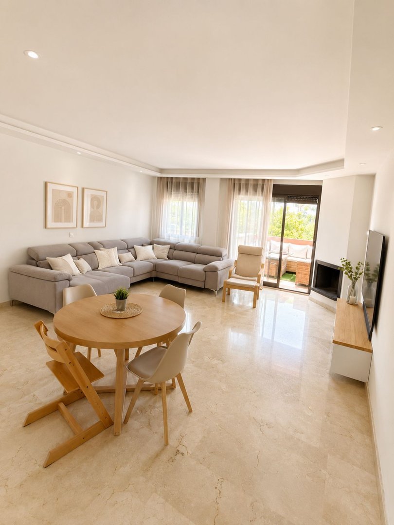 Modern living and dining area with a sectional sofa, round table, and access to a sunny terrace with outdoor seating.
