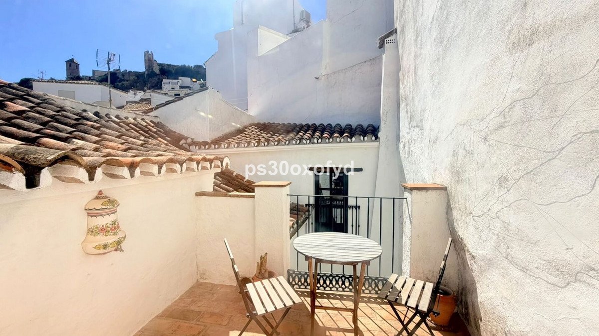 A small balcony with a table and chairs, overlooking a Spanish village with a castle on the hill.
