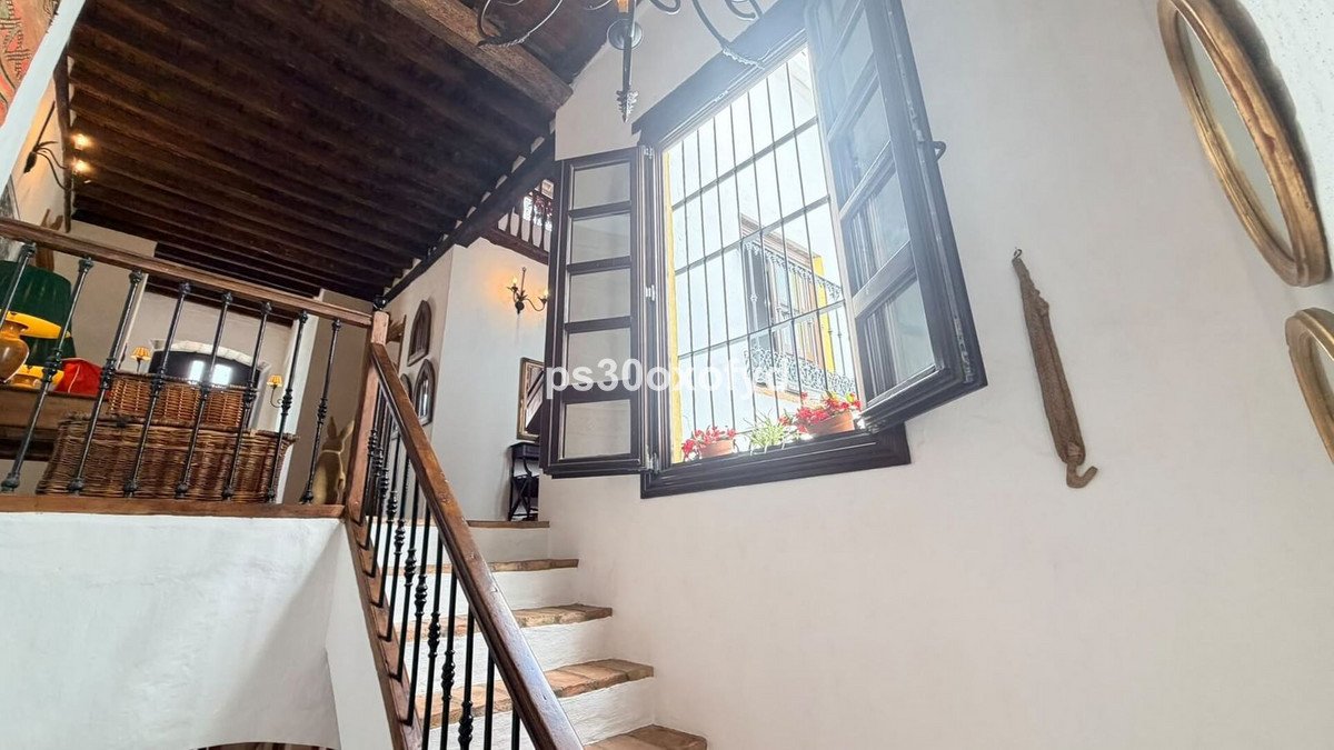 Interior staircase with wooden beams, a large window with an outdoor view, and decorative elements on the wall.