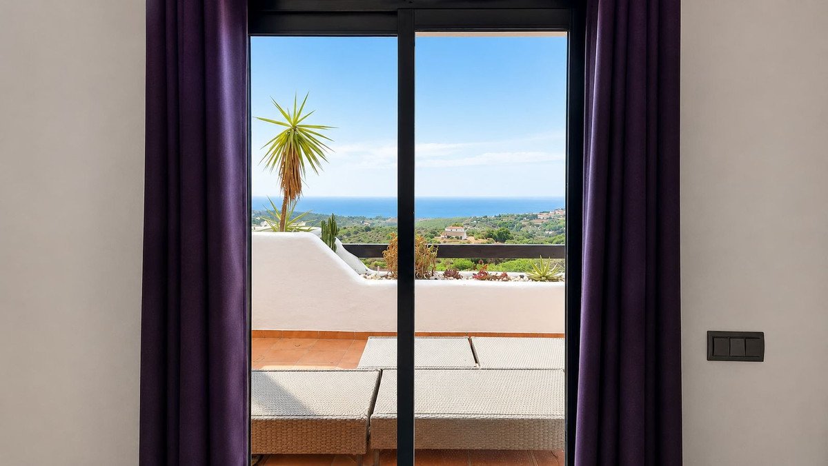 View from a room through a sliding glass door onto a terrace with sun loungers and a beautiful sea view.