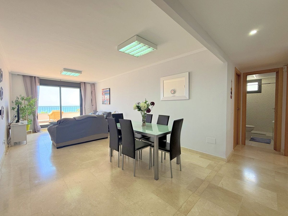 Open-plan living and dining area with a glass table, sofa, and a large window offering a sea view and balcony access.