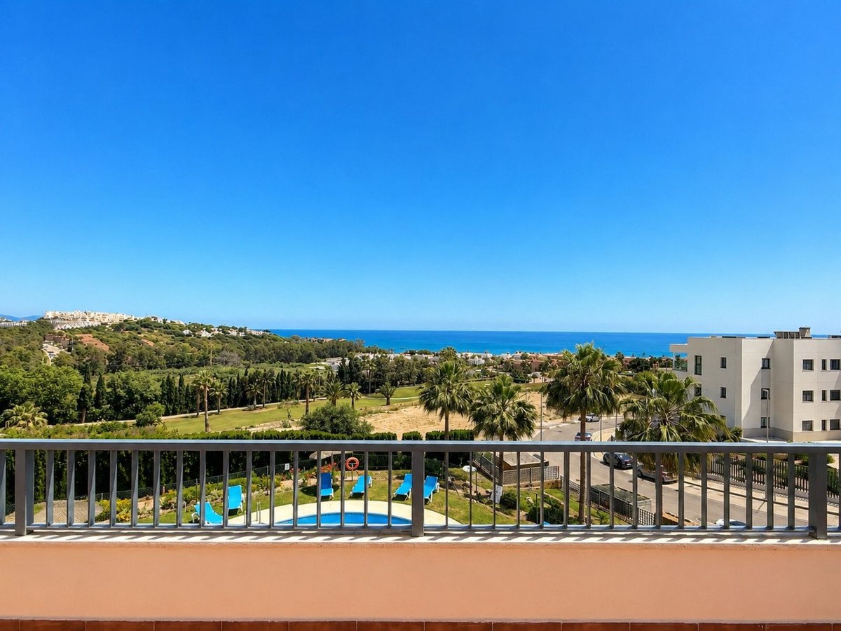 Balcony view overlooking a swimming pool, palm trees, golf course, and the Mediterranean Sea on a sunny day.