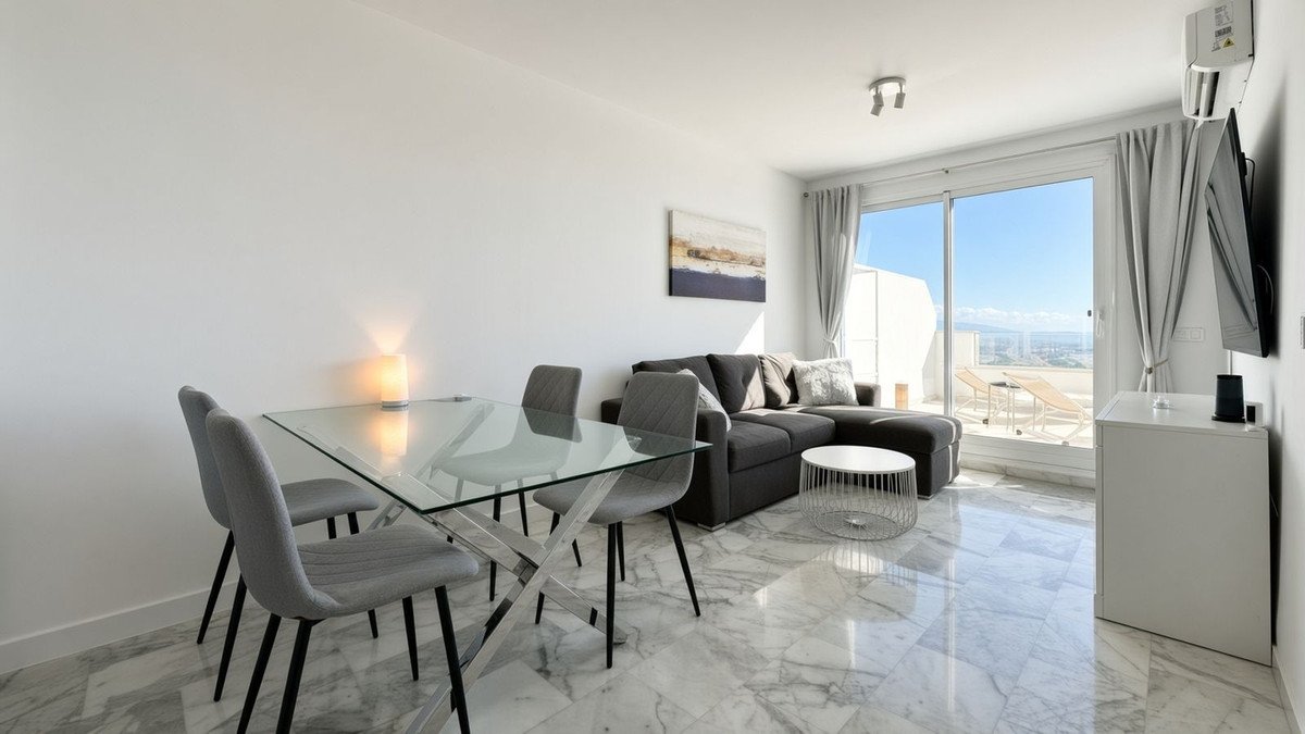 Modern living and dining area with a sectional sofa, glass table, and balcony with sea and city views.