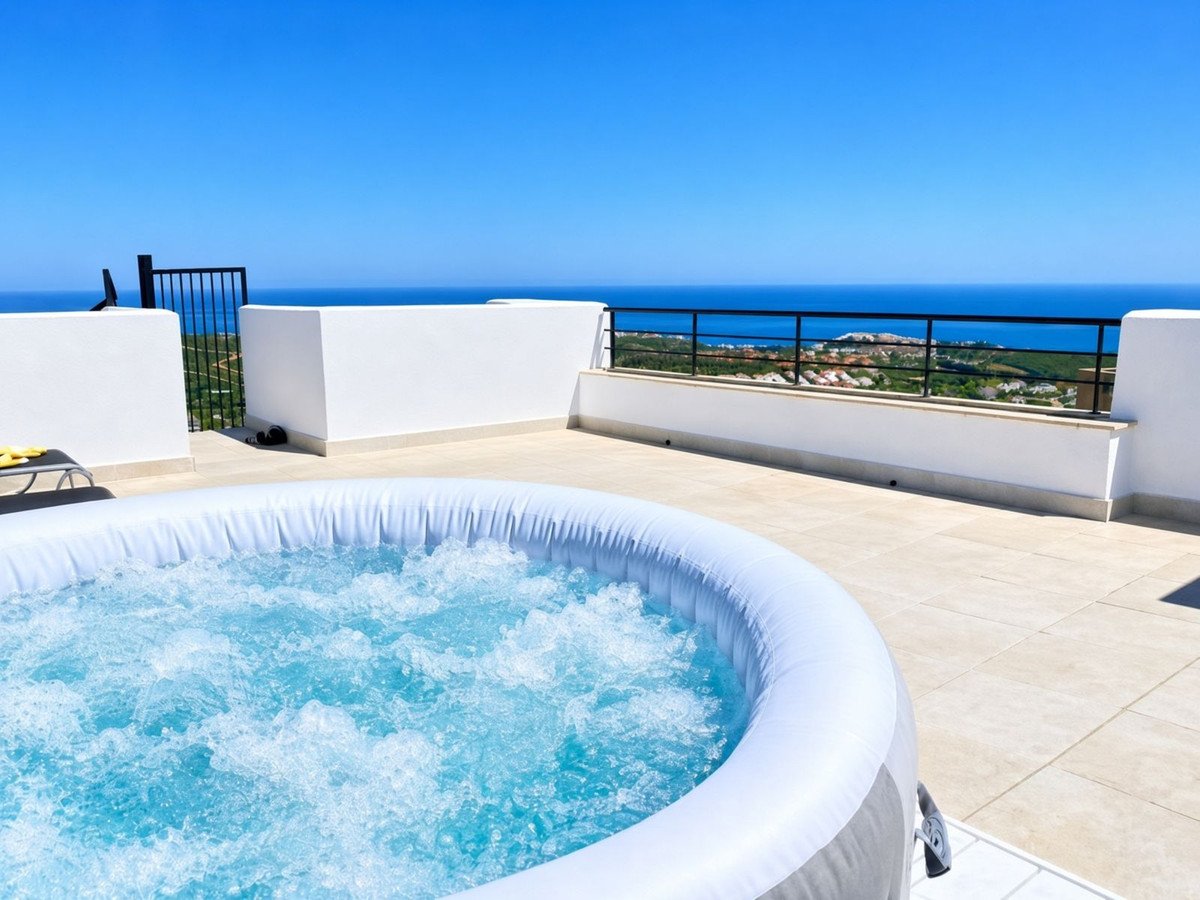 Inflatable hot tub on a terrace with a stunning sea view and distant coastal town, under a clear blue sky.