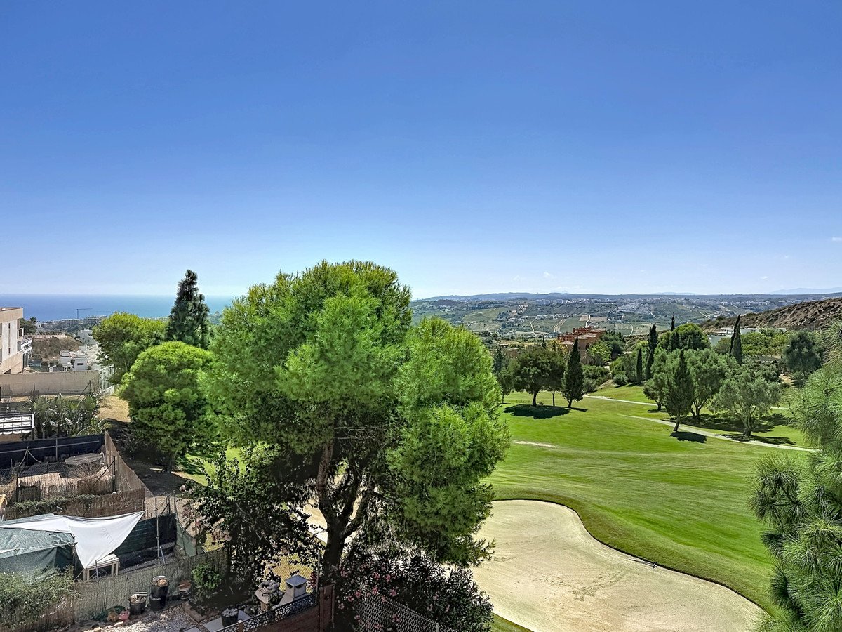 View from a balcony overlooking a golf course with trees, rolling hills, and the sea in the distance.