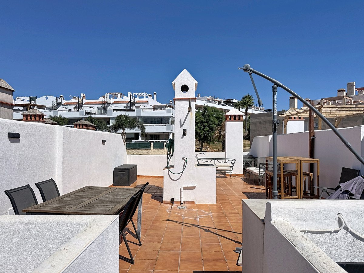 Rooftop terrace with dining furniture, BBQ, and views of white buildings under a clear blue sky.