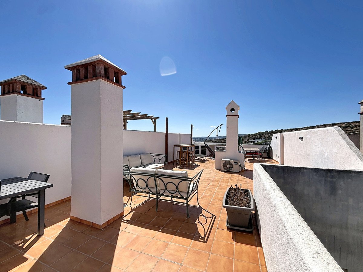Spacious terrace with seating areas, dining table, chimneys, and sea view under a clear blue sky.