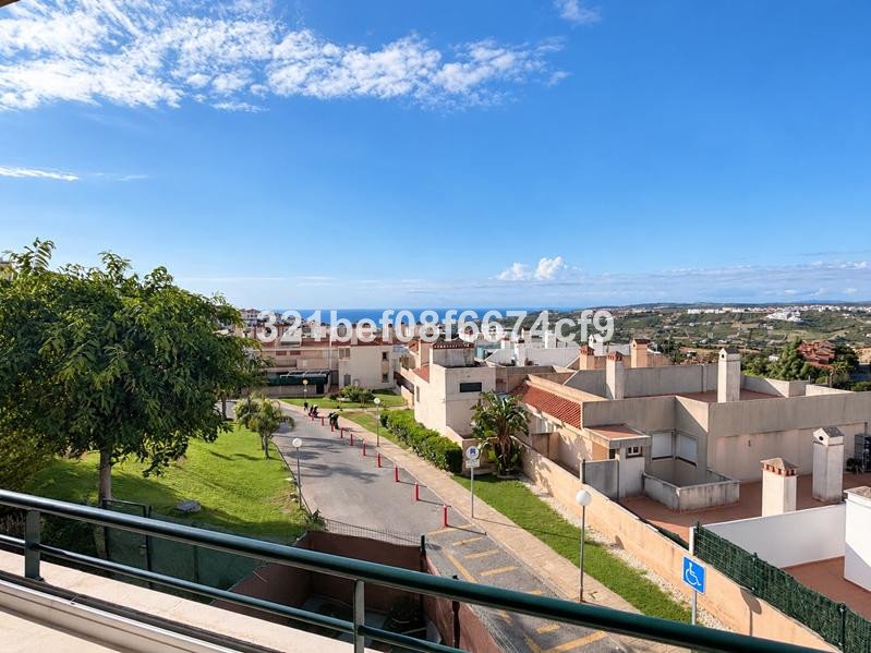View from a balcony overlooking a residential complex with the sea and hills in the distance under a blue sky.