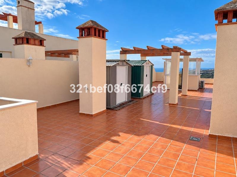 A spacious rooftop terrace with terracotta tiles, chimneys, storage sheds, and a distant view of the sea under a blue sky.