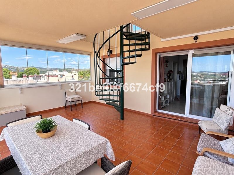 A tiled terrace with a dining table, chairs, a spiral staircase, and large windows offering views of a town and hills.