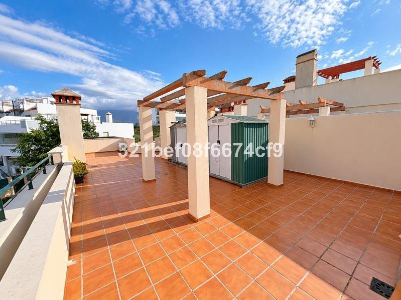 Spacious tiled terrace with a wooden pergola, a storage shed, and views of buildings and sky.