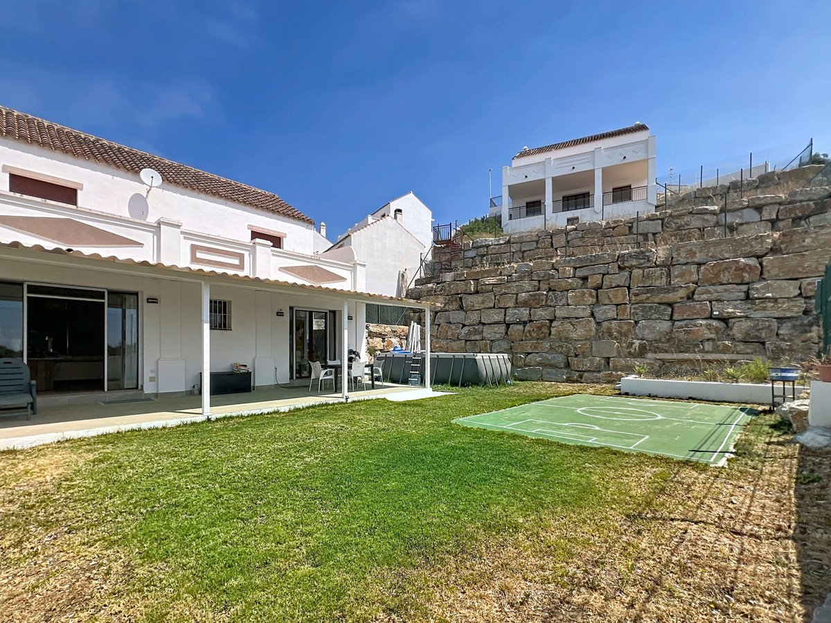 Outdoor space with a small pool, a sports court, and a large stone wall on a sunny day.