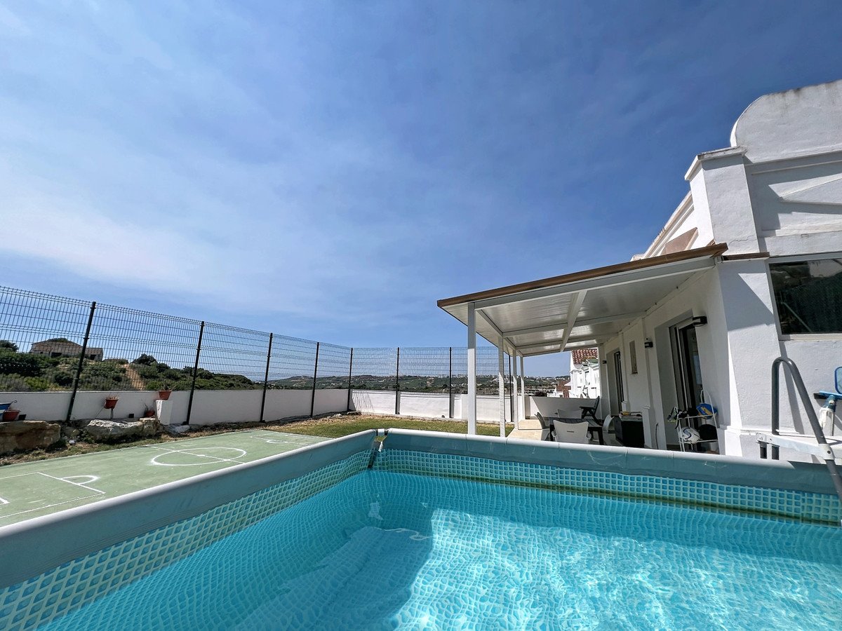Swimming pool and multi-sport court with a covered patio and seating area outside a white house on sunny day.