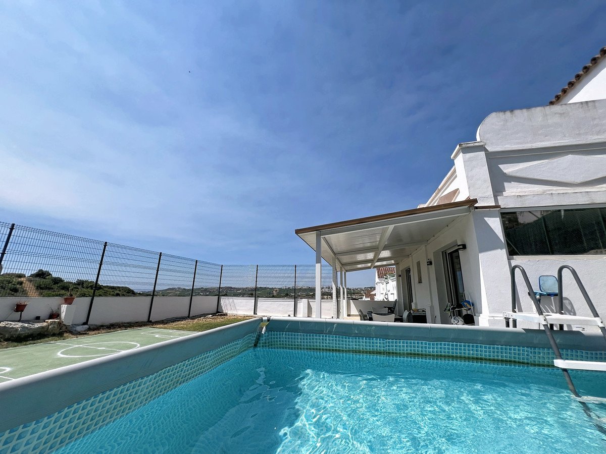 A swimming pool with a tennis court next to it, a covered patio and a white building under a blue sky.