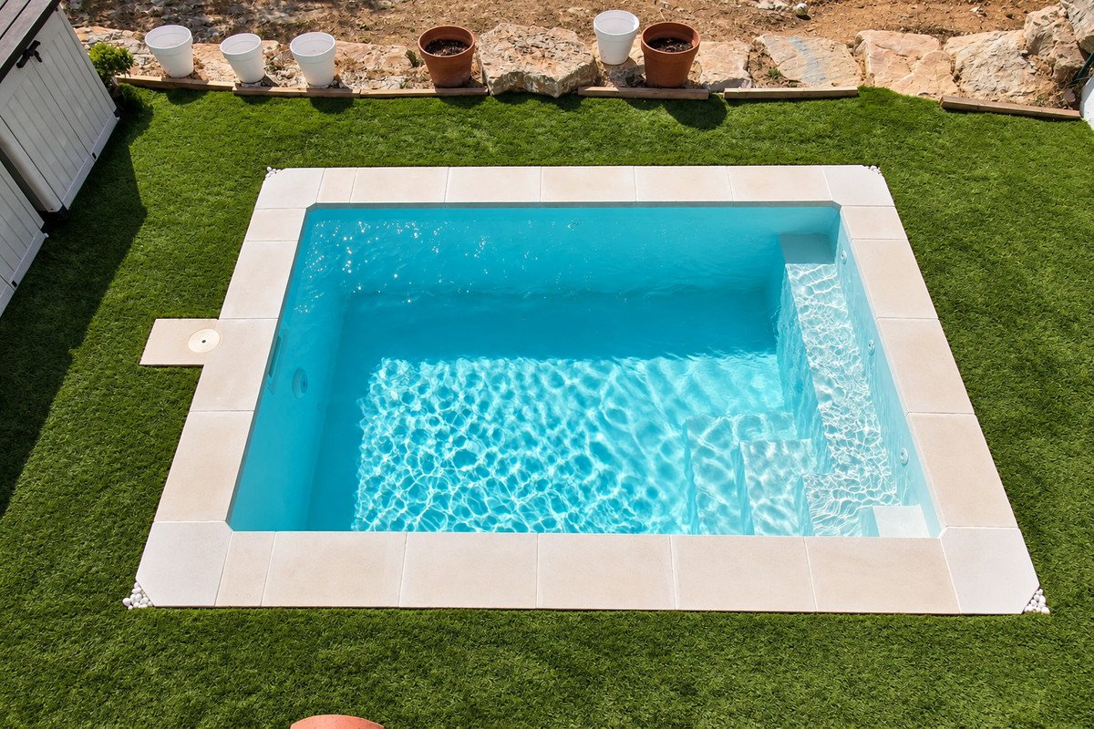 An inviting swimming pool with steps, surrounded by lush green artificial grass and stone tiling.