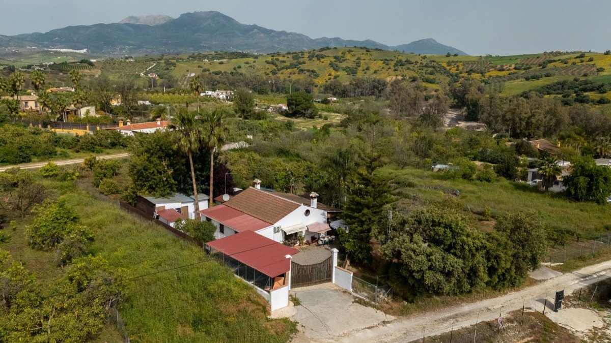 Aerial view of a white villa with red roof, surrounded by green hills and mountains in the background.