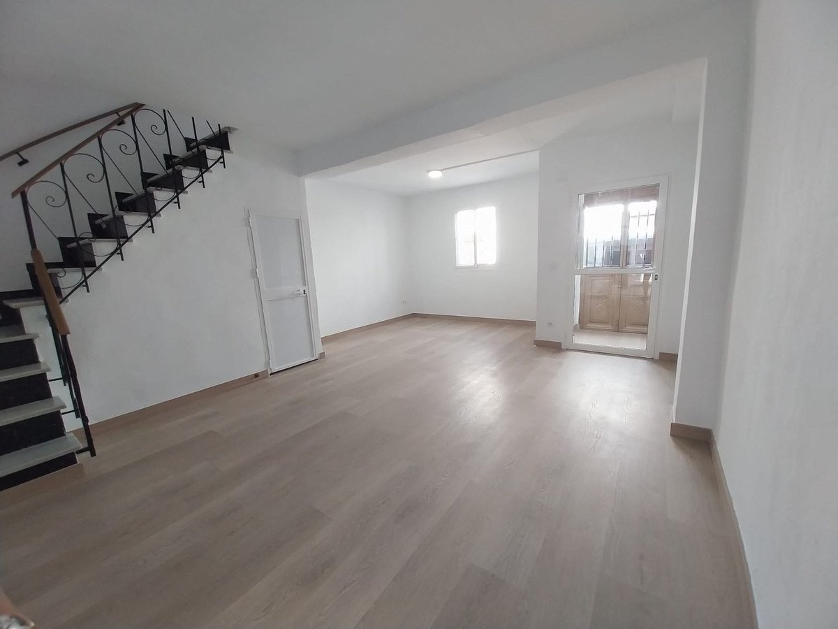 Empty room with light wood flooring, white walls, and a staircase with black metal railing.