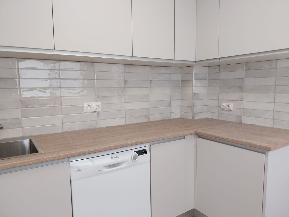 Modern kitchen with white cabinets, wooden countertops, and tiled backsplash.