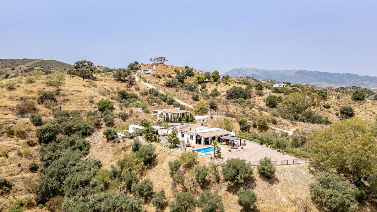 Modern villa with pool on hillside, panoramic mountain views, surrounded by dry landscape and olive trees.