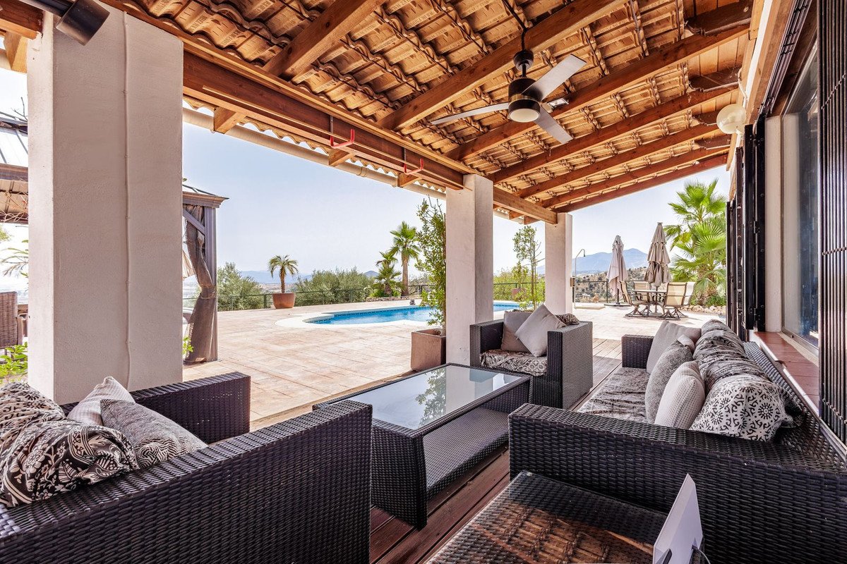 Covered outdoor lounge area with wicker furniture and a swimming pool in the background