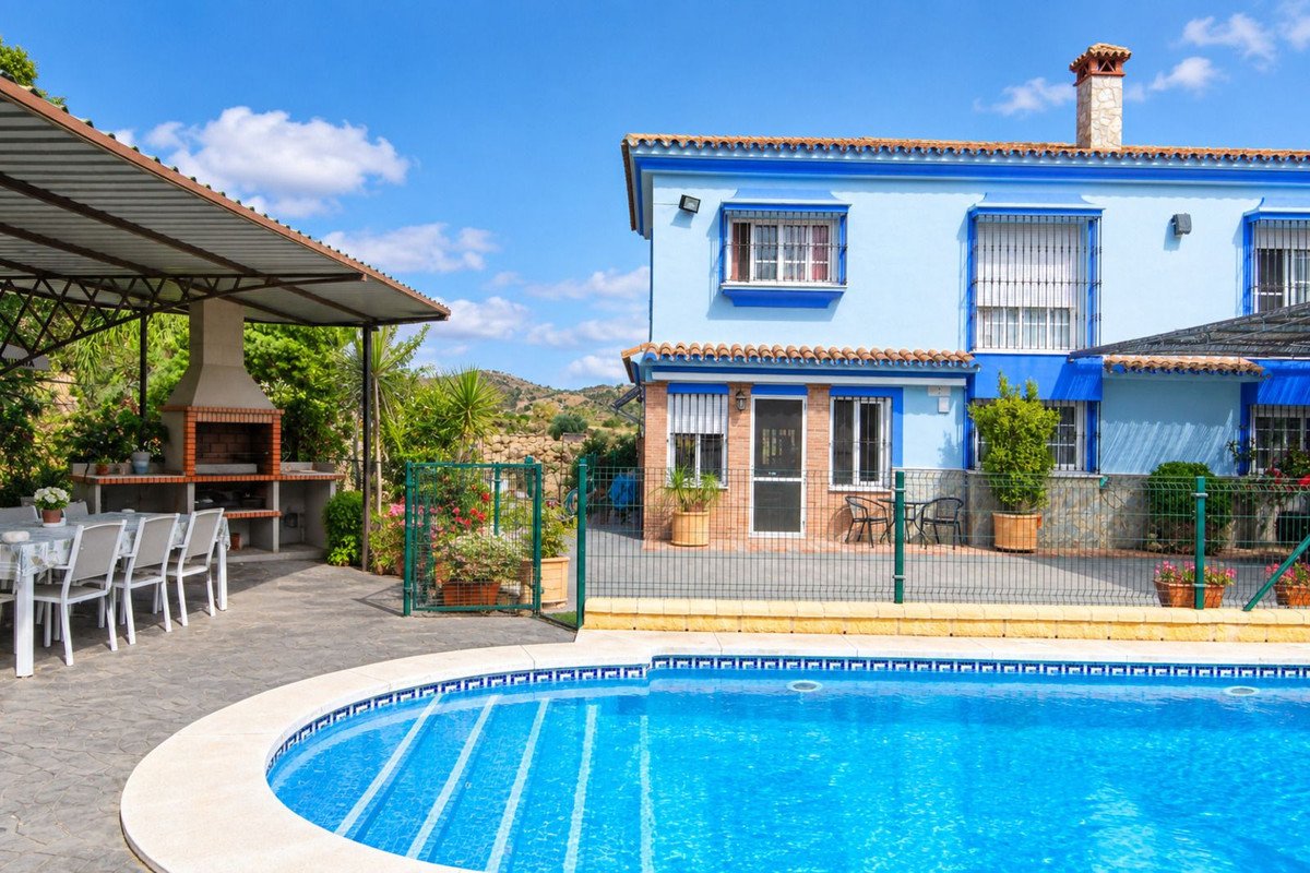 Blue villa with swimming pool, outdoor dining area, and built-in barbecue on a sunny day.