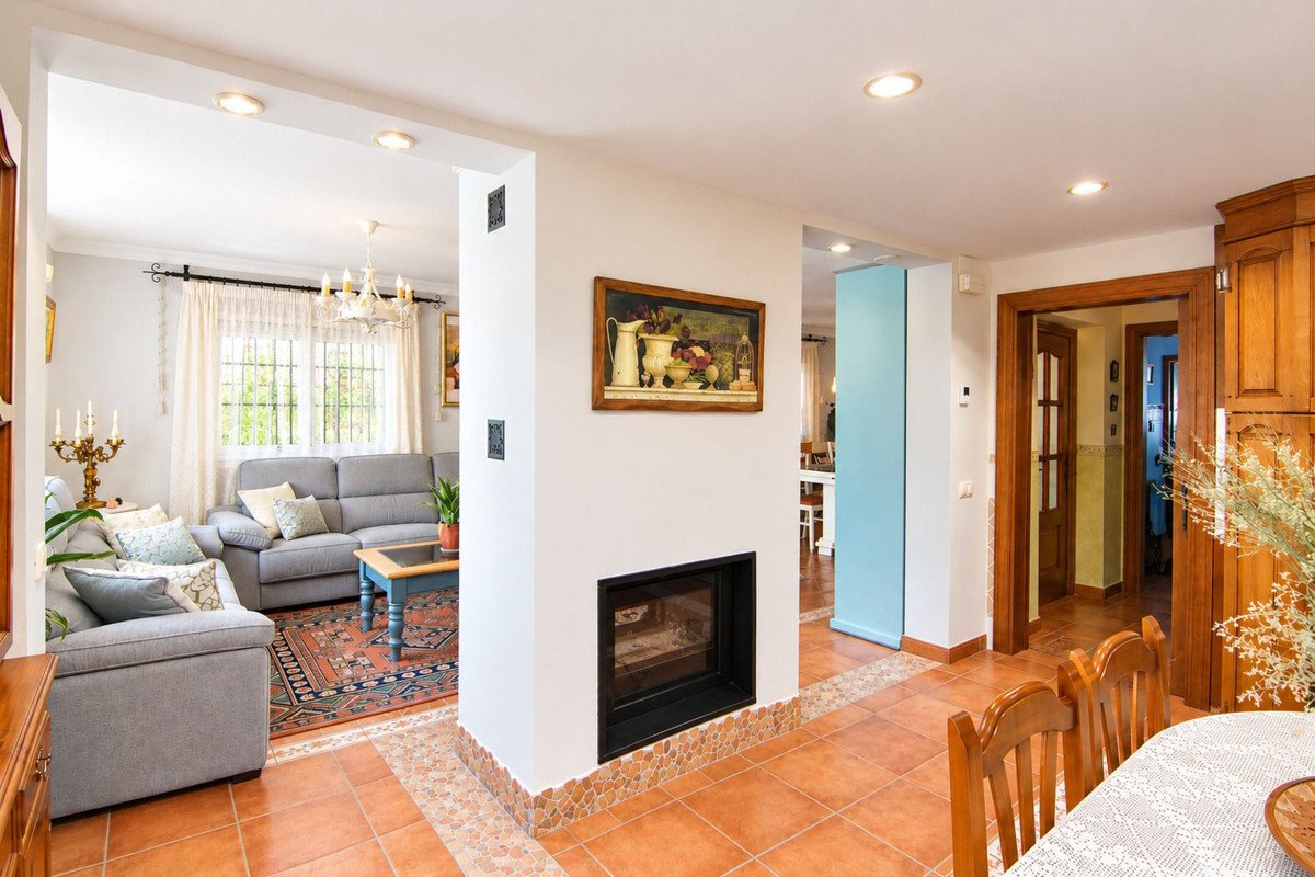 Living room with fireplace, connected to a dining area and view of hallway and kitchen cabinets.