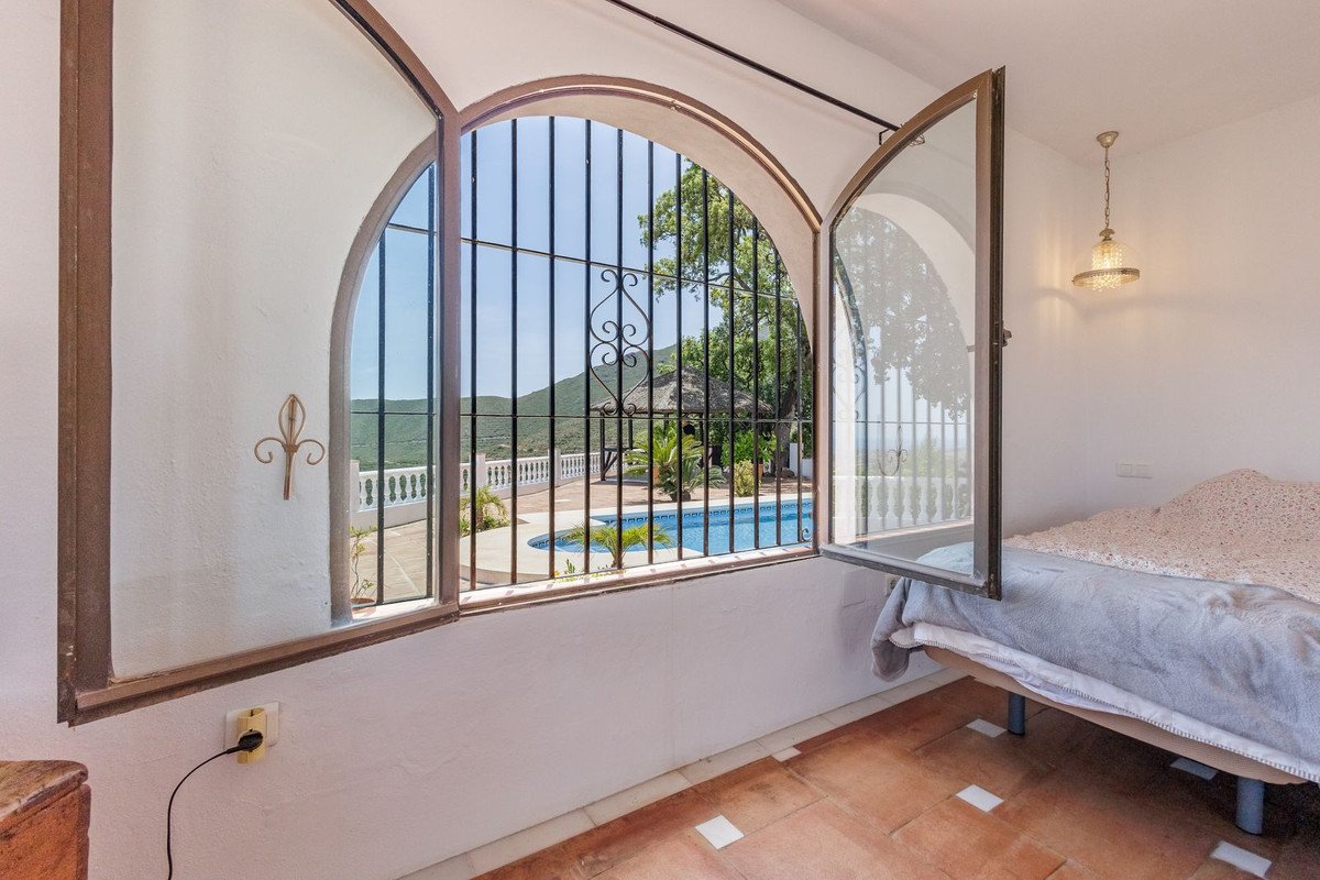 Sunlit bedroom with large arched windows overlooking a swimming pool and garden