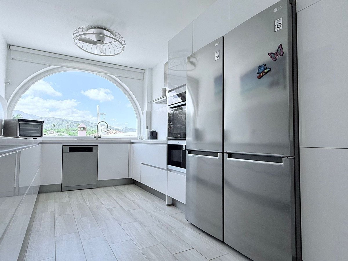 Modern kitchen with stainless steel appliances, white cabinetry, and an arched window offering mountain views.