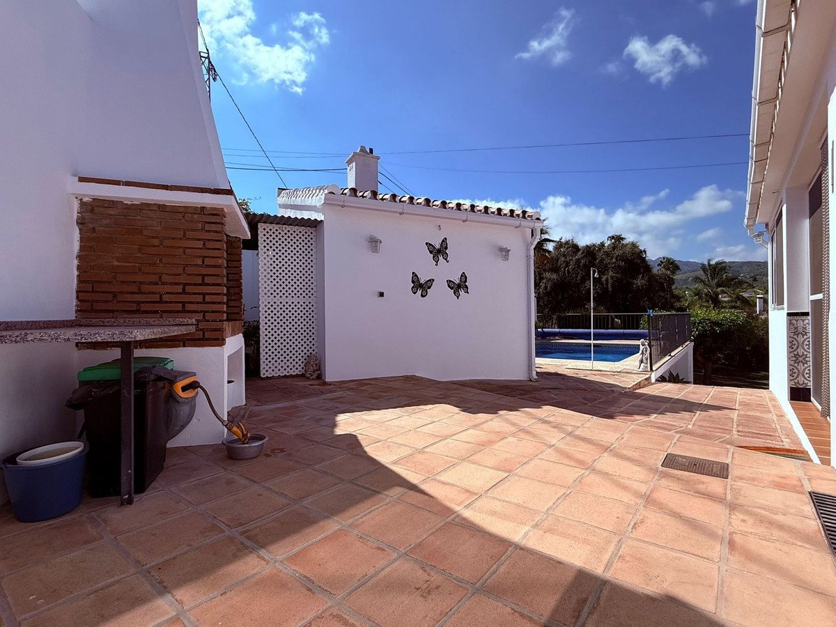 Terracotta patio with outdoor kitchen, pool view, and butterfly wall art under blue sky.