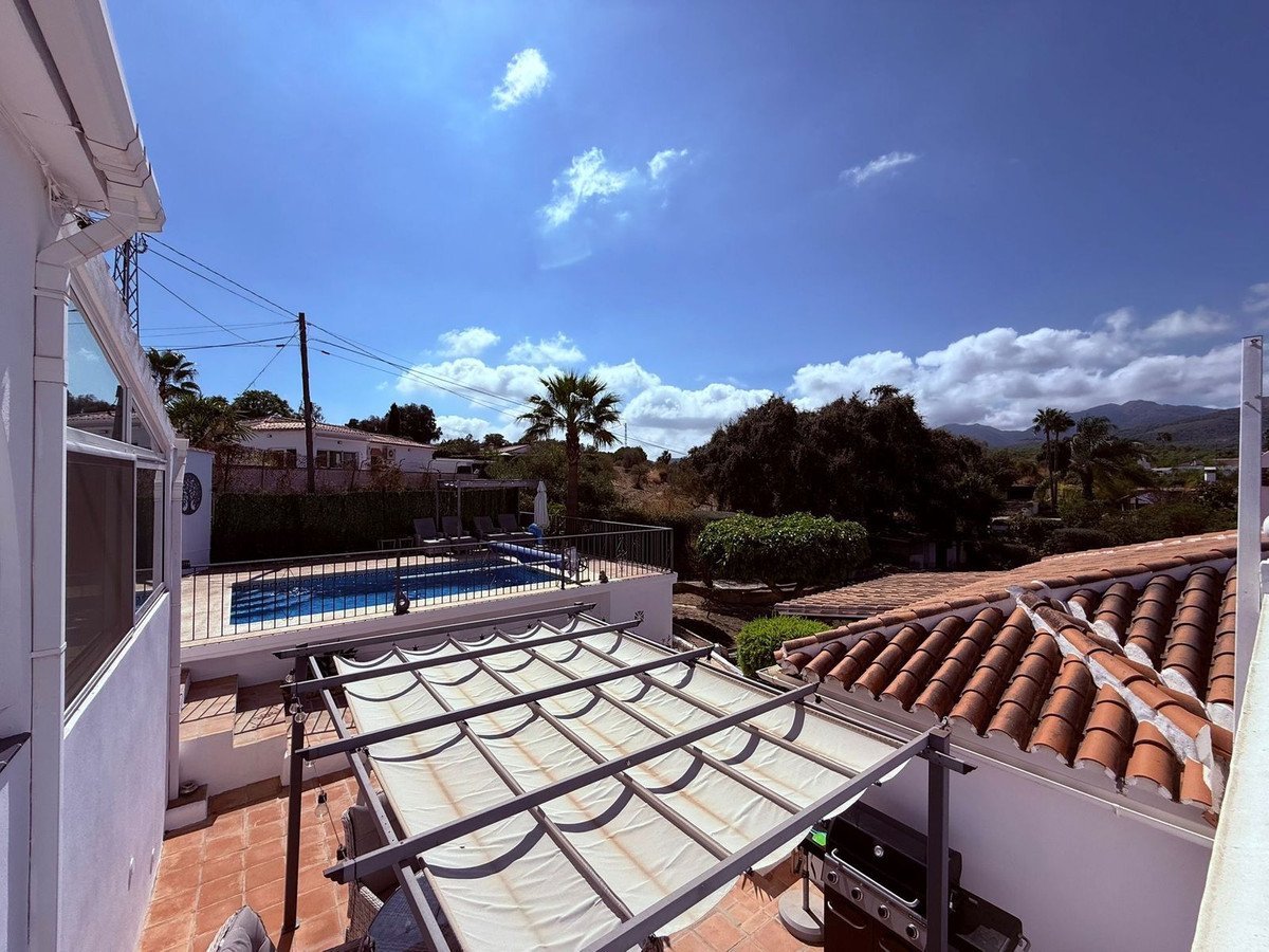 Terrace with pool view, tiled roof, and mountain backdrop under blue sky.
