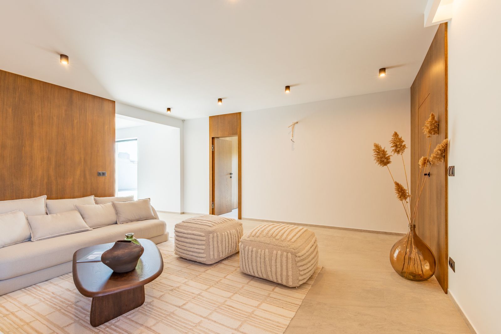 Moderne woonkamer met beige bank, poefs en houten accenten.