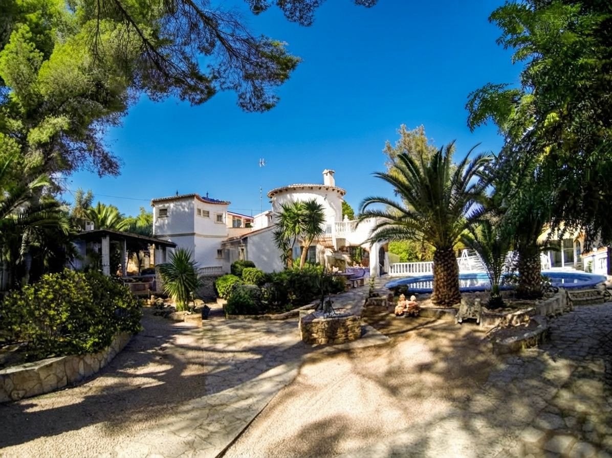 A large white villa with palm trees and a swimming pool in the garden on a sunny day.
