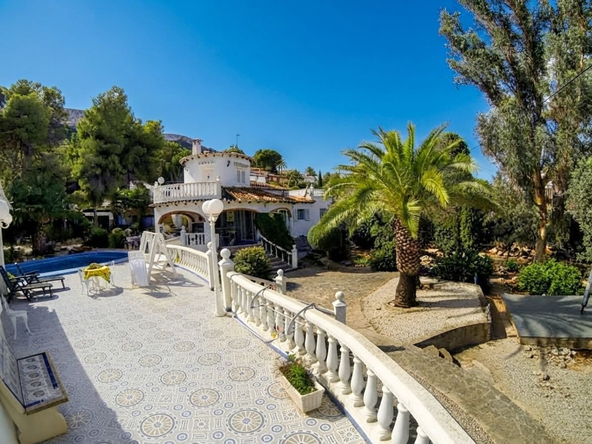 Outdoor patio with a swimming pool, palm tree, and a white villa in the background on a sunny day.