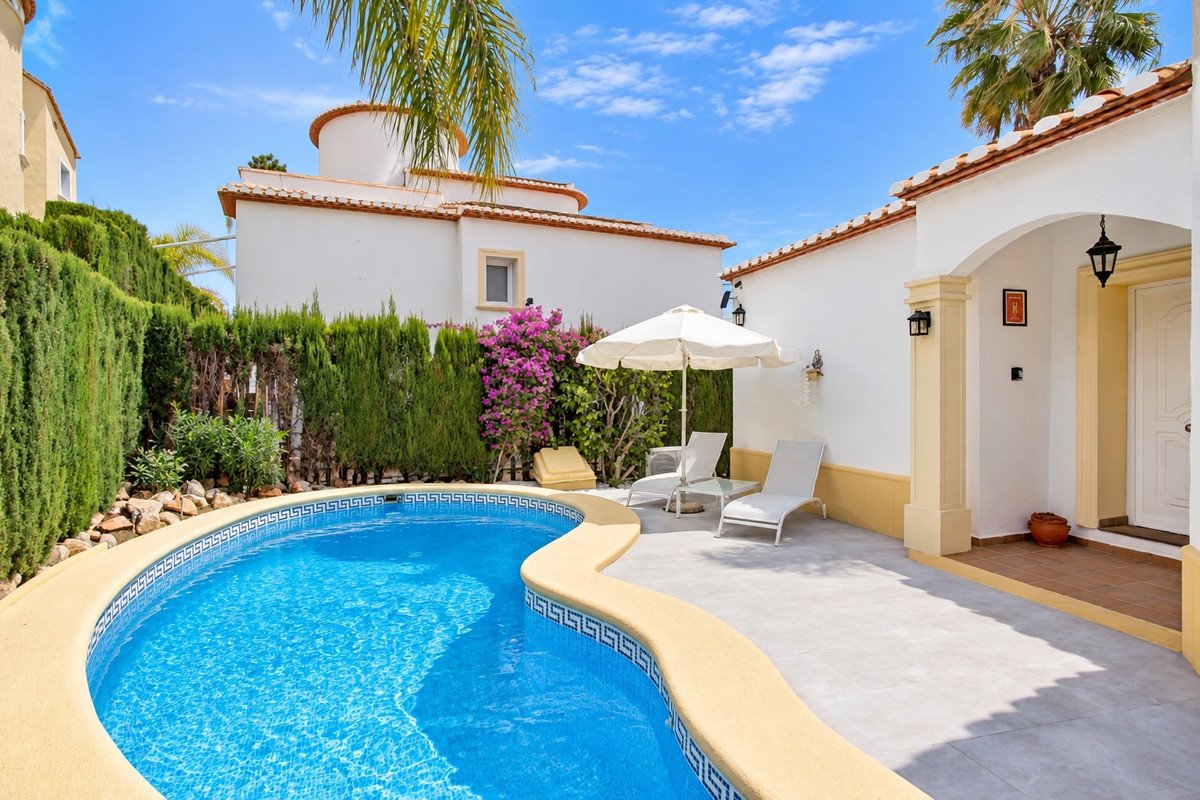 A private swimming pool with sun loungers and an umbrella on a sunny patio area with lush green hedges.