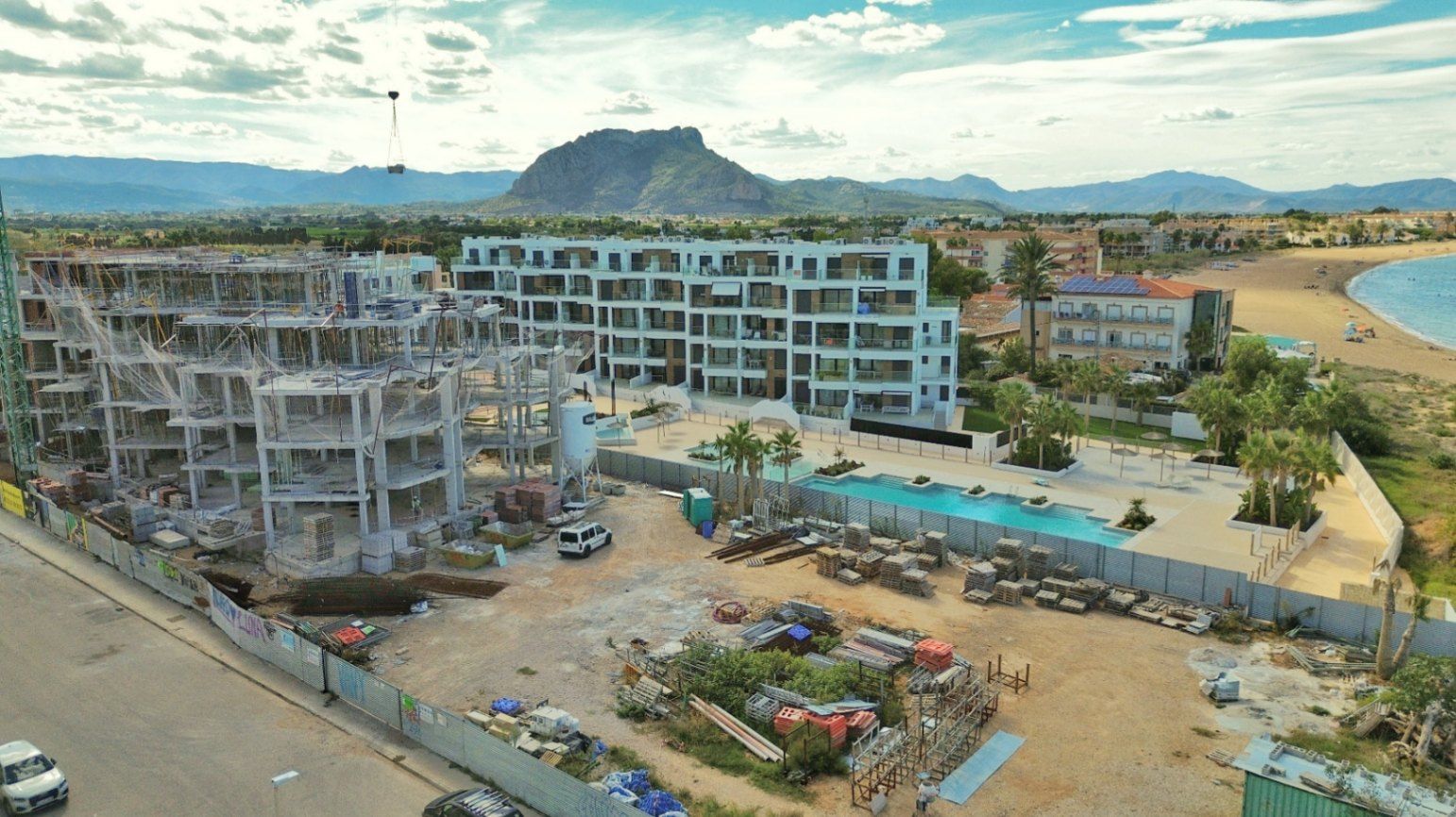 Nieuwbouw appartementencomplex aan de kust in aanbouw, met zwembad en uitzicht op de bergen.