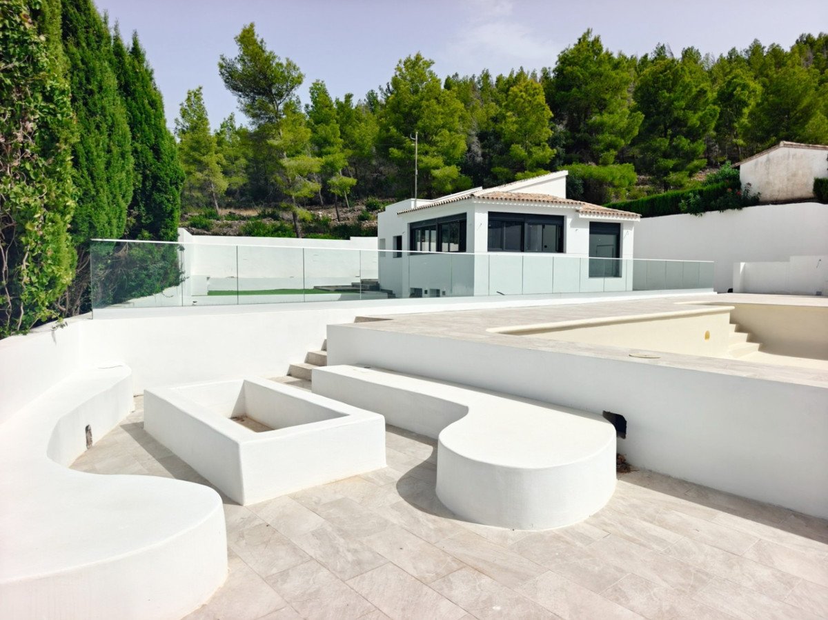 Modern white villa with an outdoor seating area, an empty swimming pool, and a forest view.