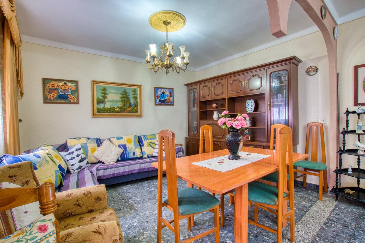 A living and dining room with a sectional sofa, dining table, wooden cabinet, and decorative paintings on the wall.