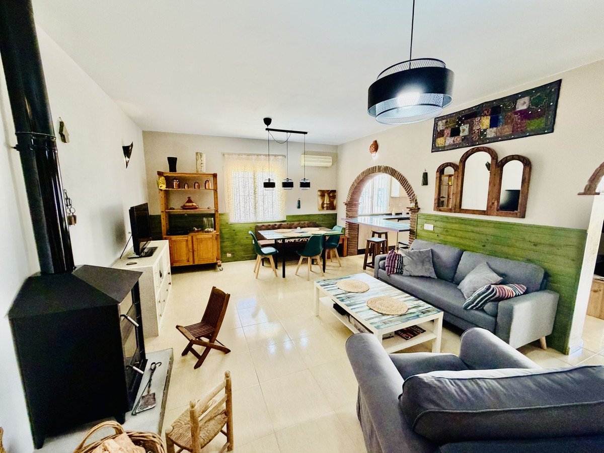Living and dining area with a fireplace, grey sofa, wooden dining table, and arched doorway to the kitchen.