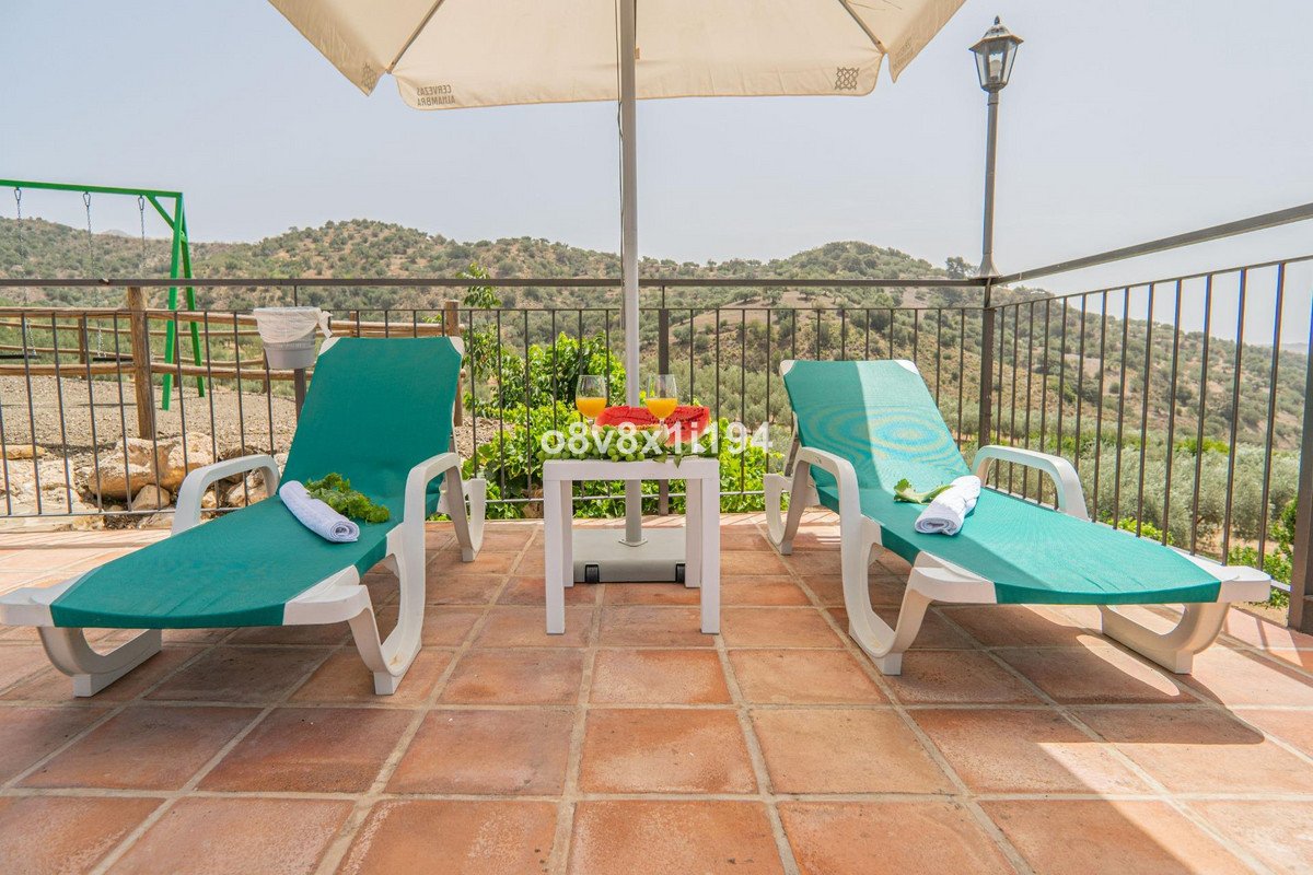 Two green lounge chairs with a small table and drinks on a tiled terrace overlooking a scenic hillside view.