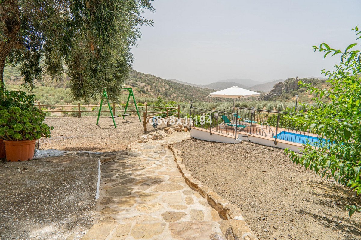 Outdoor area with a swimming pool, sun loungers, umbrella, and a swing set, overlooking a valley with rolling hills.