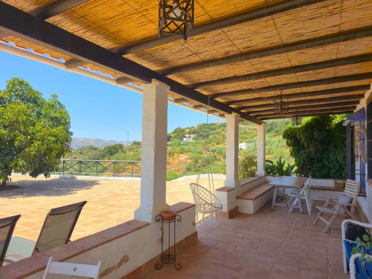 Covered terrace with seating area, outdoor furniture, and a scenic view of rolling hills and trees under a clear blue sky.