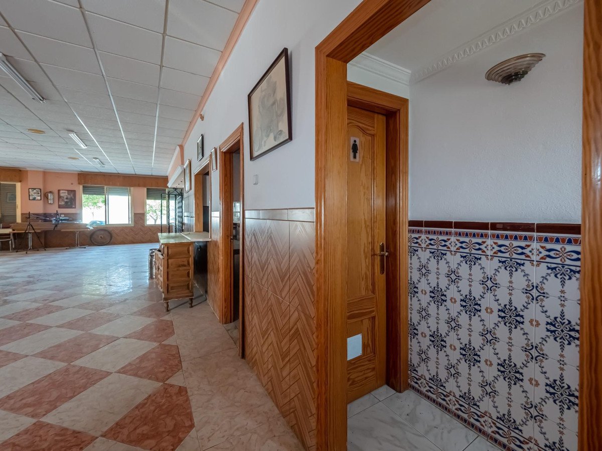 Interior hallway with wooden doors and decorative tiled walls, leading to a large room.