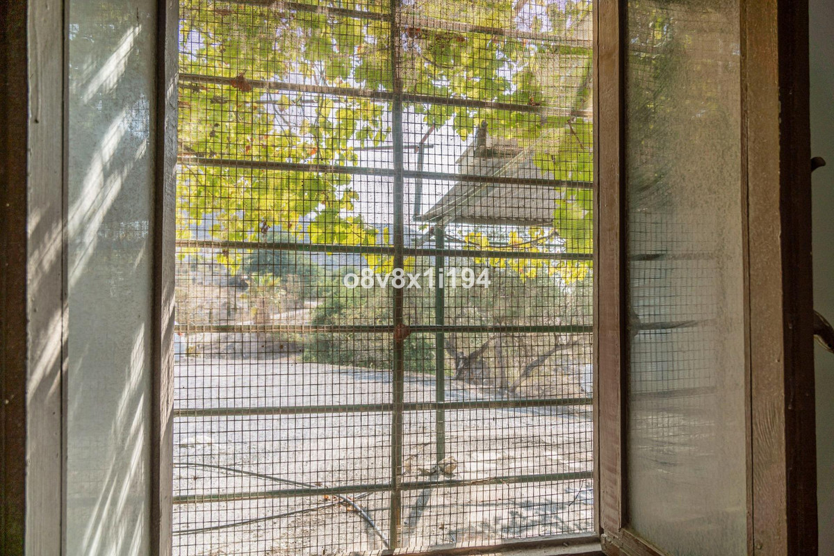 Uitzicht vanuit een raam met tralies op buitenbomen.