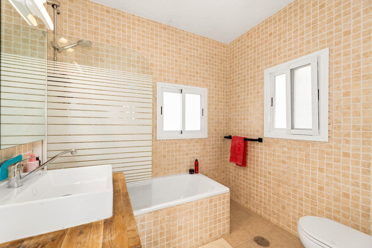 Badkamer met beige tegels, ligbad, wastafel en houten blad.