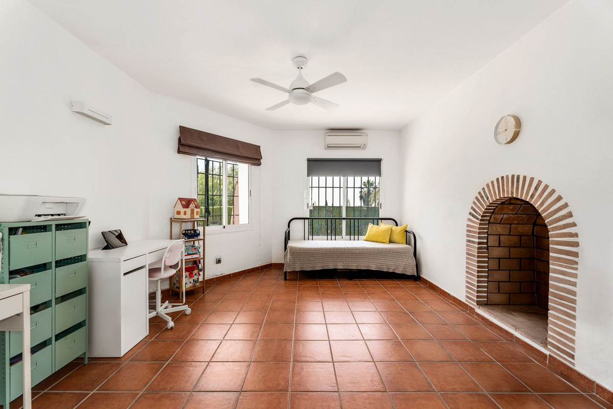 Lichte kamer met terracotta tegels, bureau, bed en open haard.